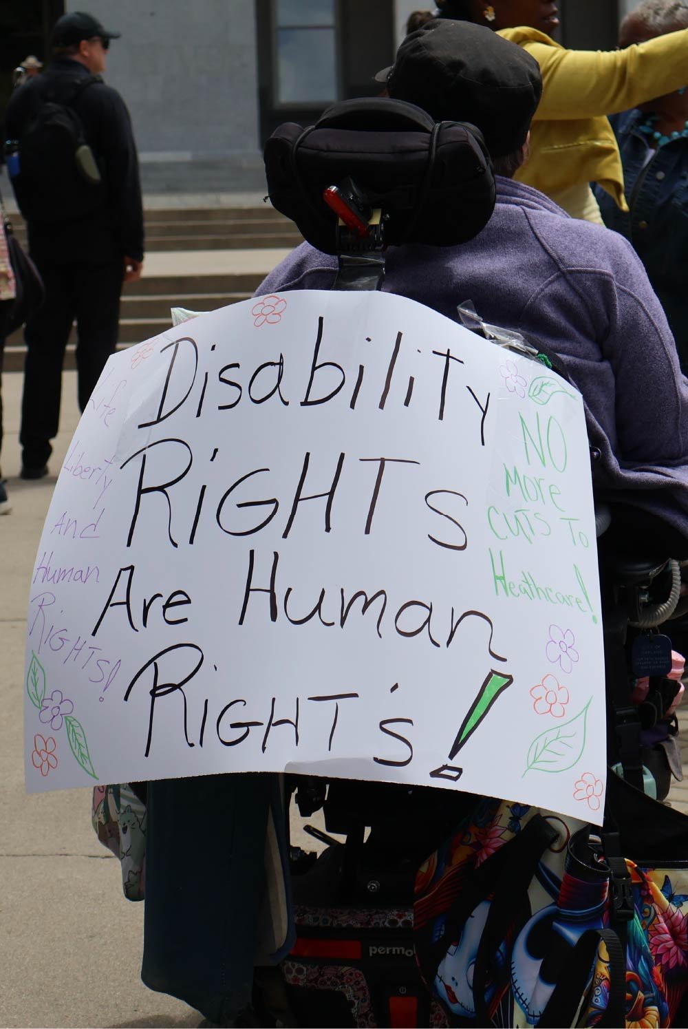 Photo of a woman at the 2026 CDLA Day of Action at the Capitol rally with a sign saying, "Disability Rights Are Human Rights!" on her powerchair.